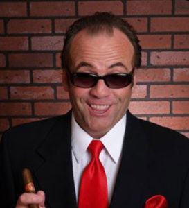 jack Nicholson celebrity impersonator caucasian male with very short black hair. wearing all black sun glasses, a black suit and a red tie.