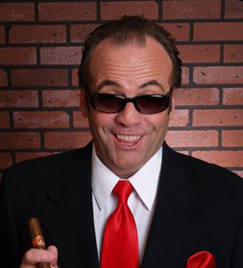 jack Nicholson celebrity impersonator caucasian male with very short black hair. wearing all black sun glasses, a black suit and a red tie.