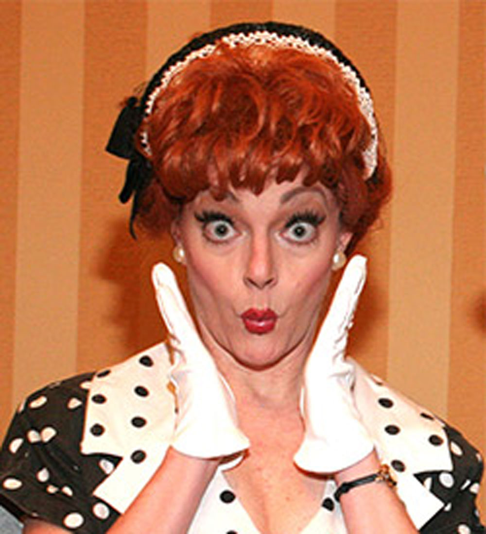 Lucille ball celebrity impersonator caucasian female with ginger red hair wearing a black and white hair band, white gloves and a polkadot dress that has a white collar with black polka dots and the rest of the dress black with white polka dots.