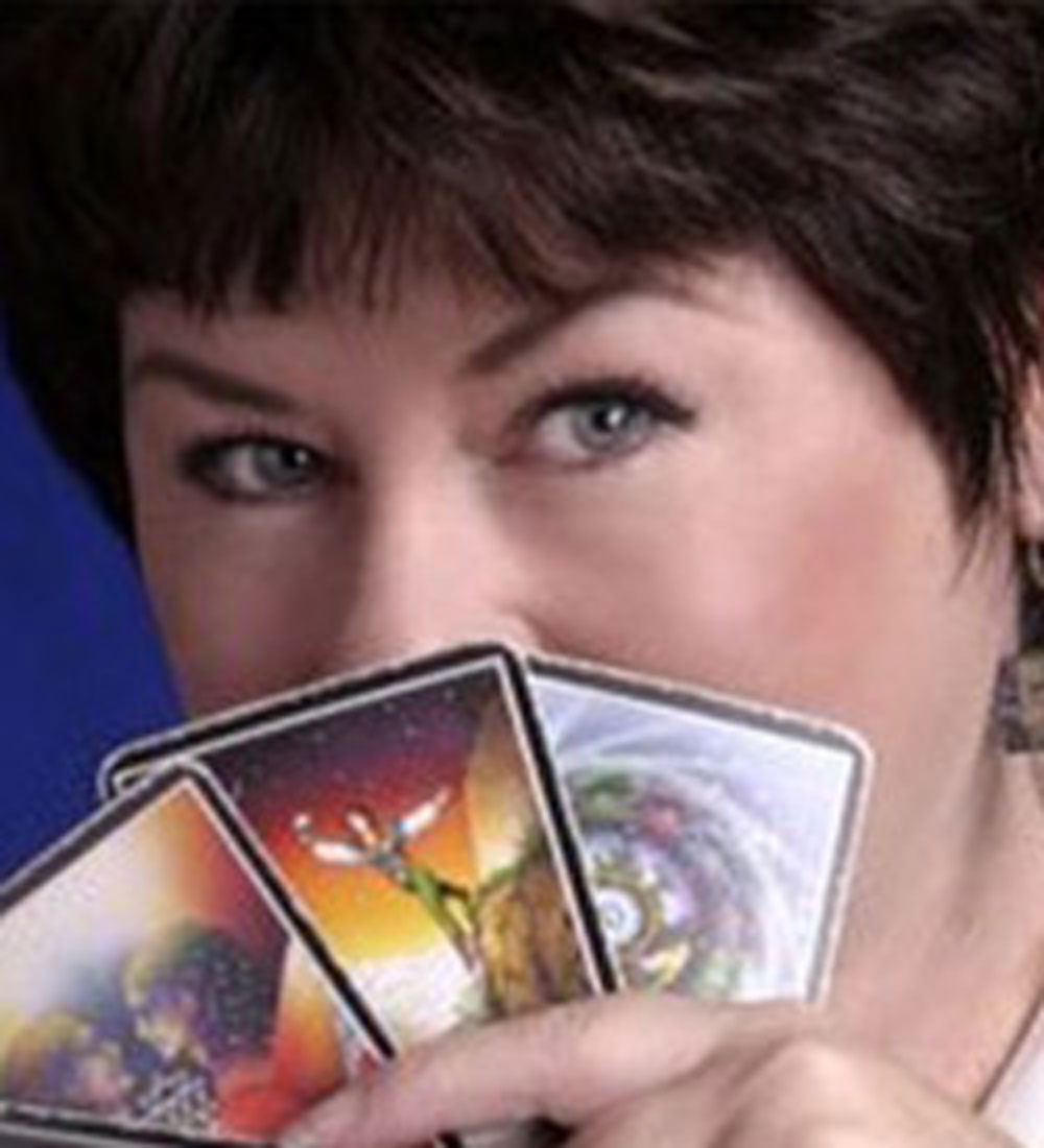 Mystic Mona caucasian female with brunette hair holding tarot cards in front of her face.