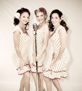 Swing City Dolls a trio of caucasian women huddled around a microphone in a classic group style.