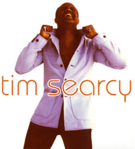 Tim searcy an african american man wearing a white collared and button down t-shirt and black pants.