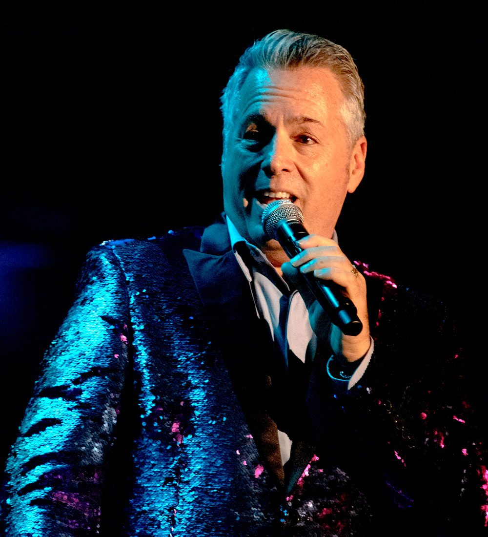Jay Josephy caucasian male with grey hair and singing into a microphone, wearing a sparkly purple suite trimmed in black.
